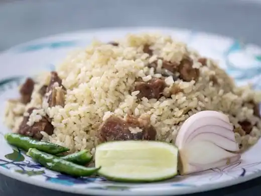 Plate of Haji beef biriyani with green chilies, lime and onion