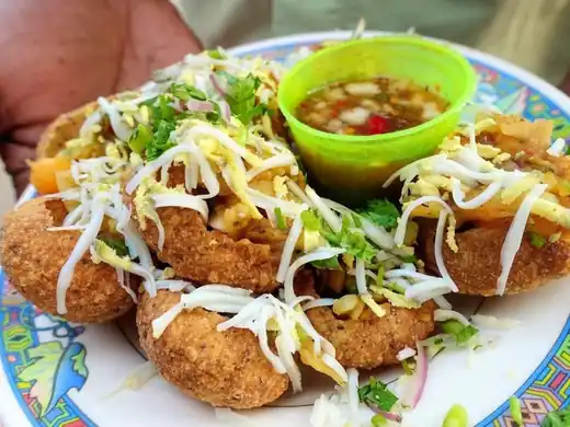 Plate of fuchka topped with grated egg and onion, with a cup of tamarind water