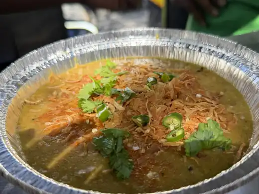 Bowl of halim topped with fried onion, coriander and green chili